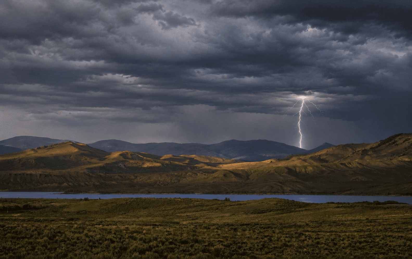 Lightning strike over reservoir and rolling hills near Kremmling, Colorado