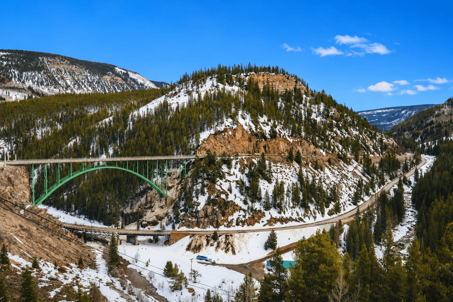 Green arch bridge spanning snowy canyon with red rock cliffs near Red Cliff, Colorado