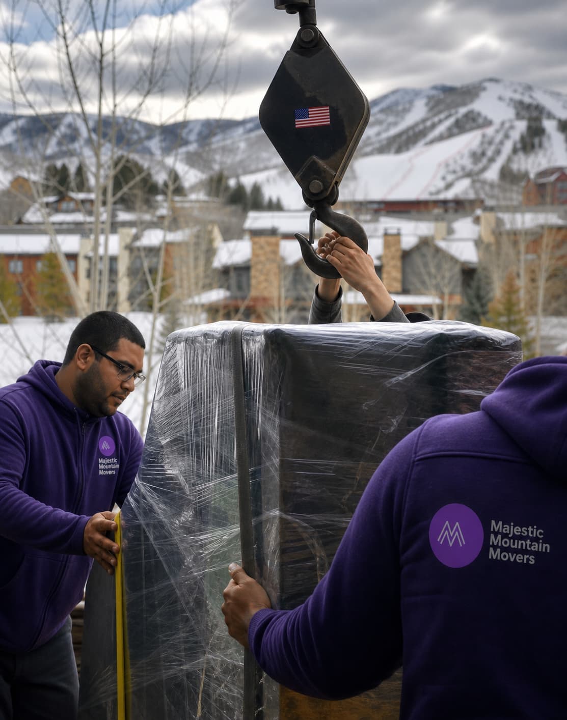 Majestic Mountain Movers crew using crane to lift wrapped piano with snowy mountains in background